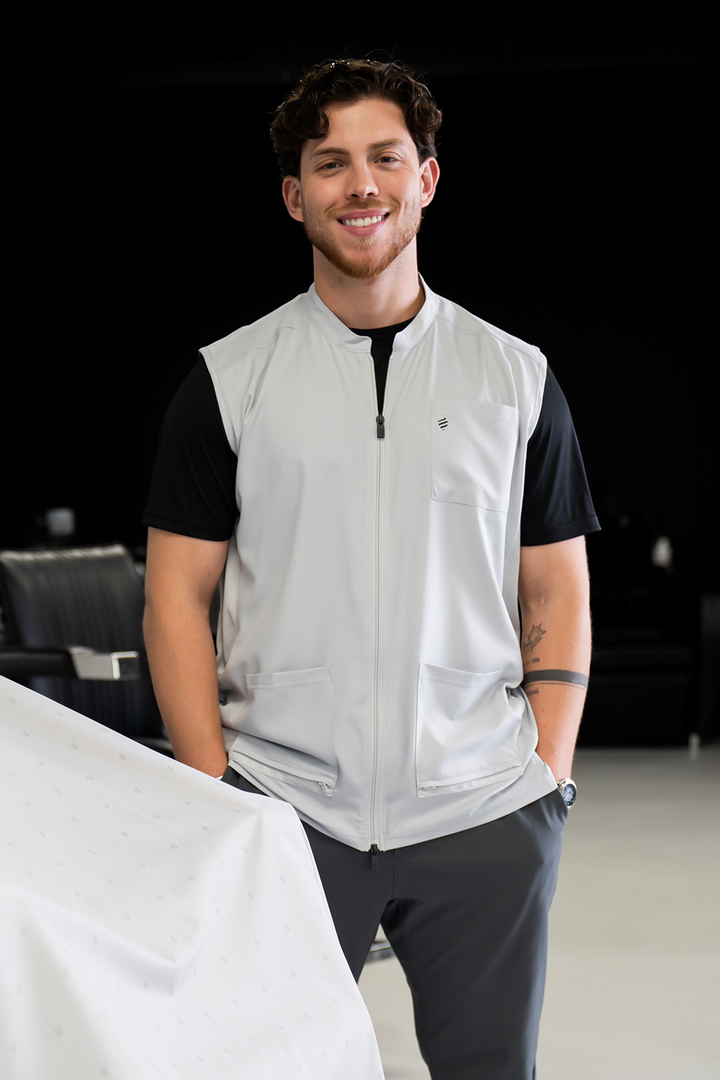Barber wearing The Barber Vest in Cool Gray over a black tee, showing the stand-up collar, chest pocket, and zippered front pockets
