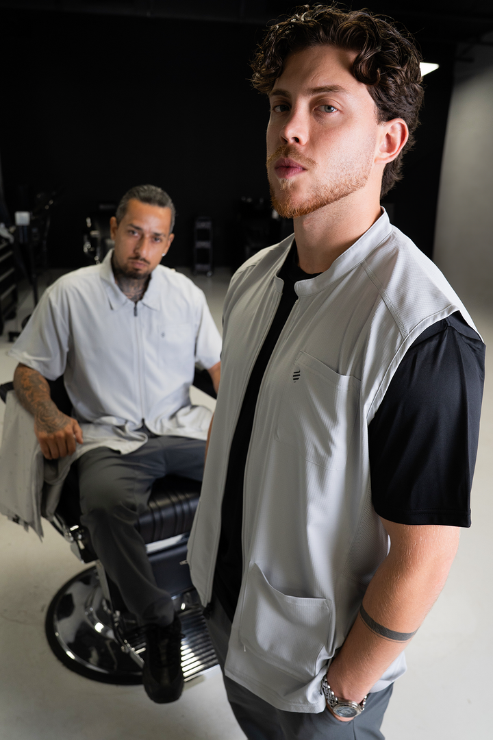 Barber in The Barber Vest in Cool Gray standing in front of a barber seated in a barber chair in a matching Cool Gray jacket